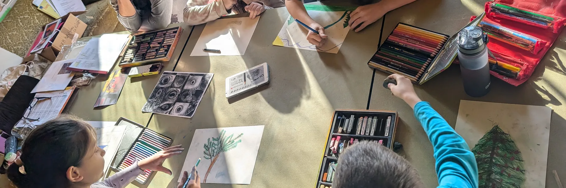 Kinder zeichnen gemeinsam an einem großen Ateliertisch